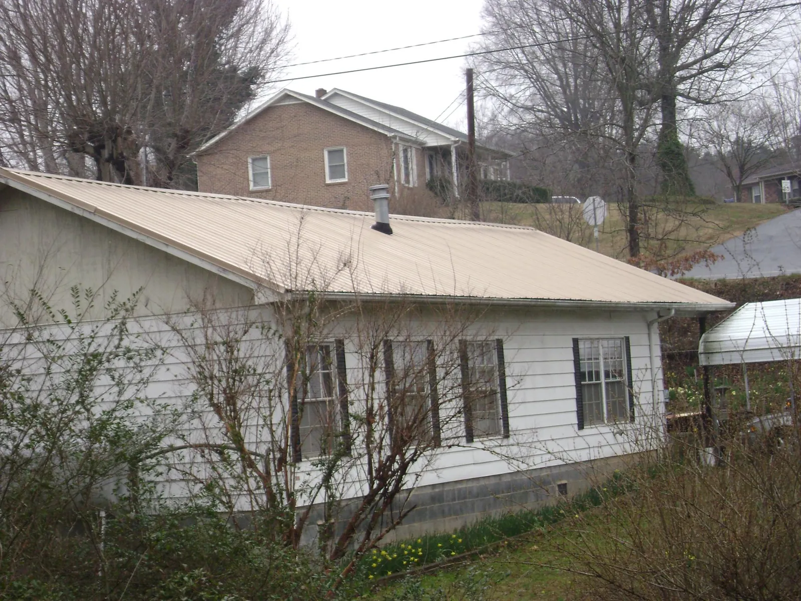 Tan metal roof on a white sided house set into a hillside — Commercial Roofing by Roofing Brothers in Warren